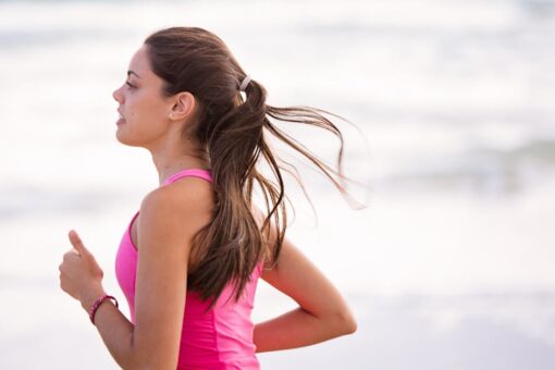 Side view of a young woman jogging on a beach wearing pink active wear.