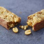 Close-up of a broken chocolate and nut energy bar on a gray surface.
