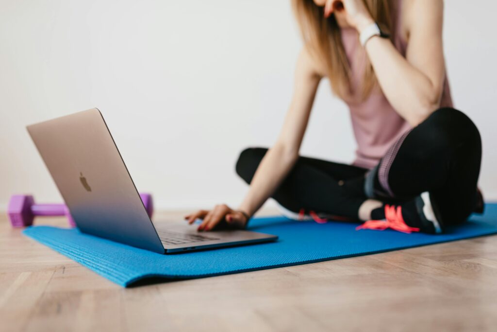 A young woman combines yoga practice with online browsing on a laptop indoors.