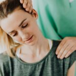 Crop professional male massage therapist in green medical uniform doing therapeutic neck massage on content female patient wearing casual clothes